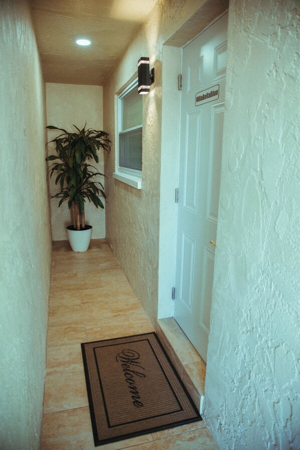 A narrow hallway with a potted plant, a welcome mat, and a door with a sign.