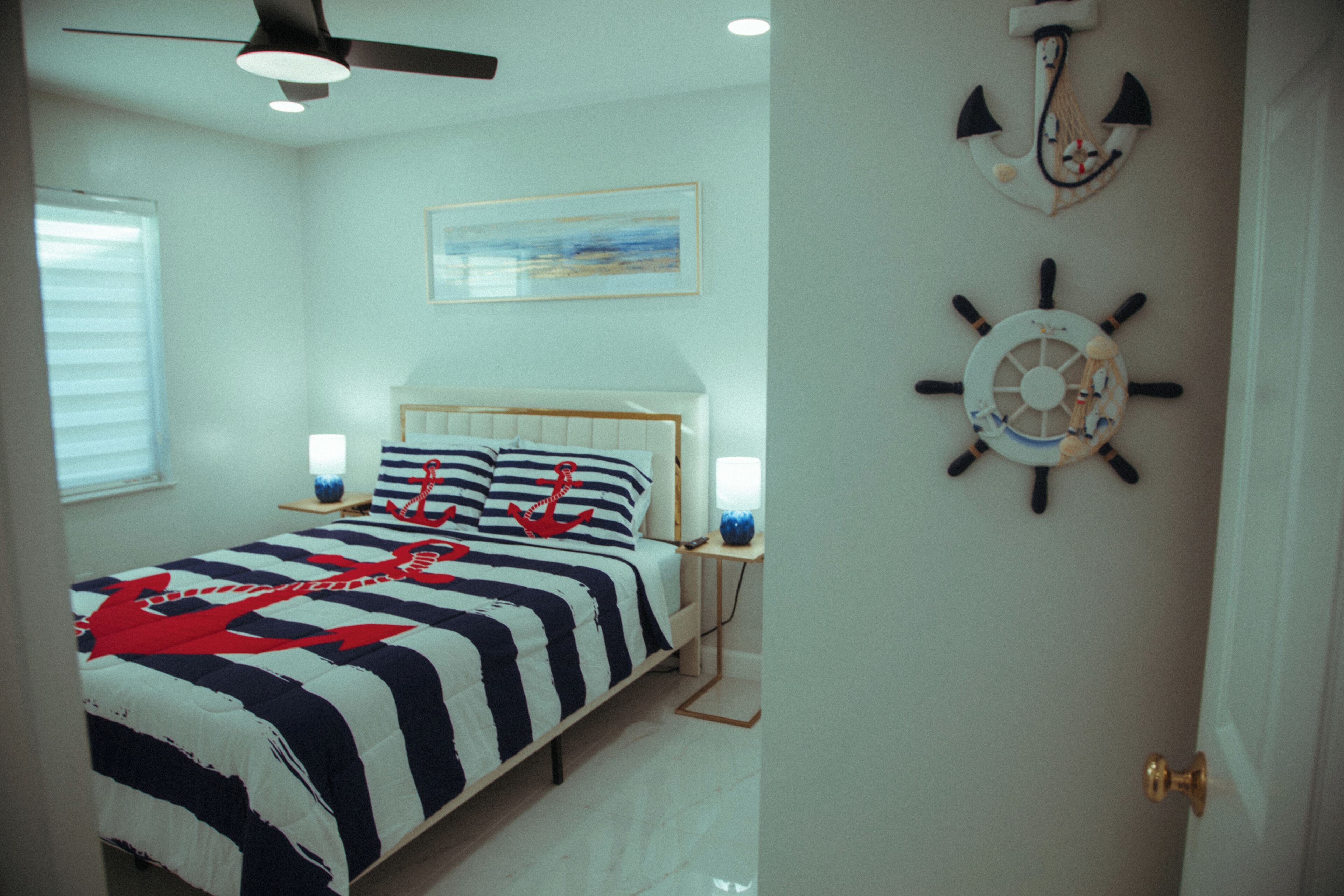Un dormitorio con una cama, un ventilador de techo, un reloj de pared y un cuadro enmarcado.
