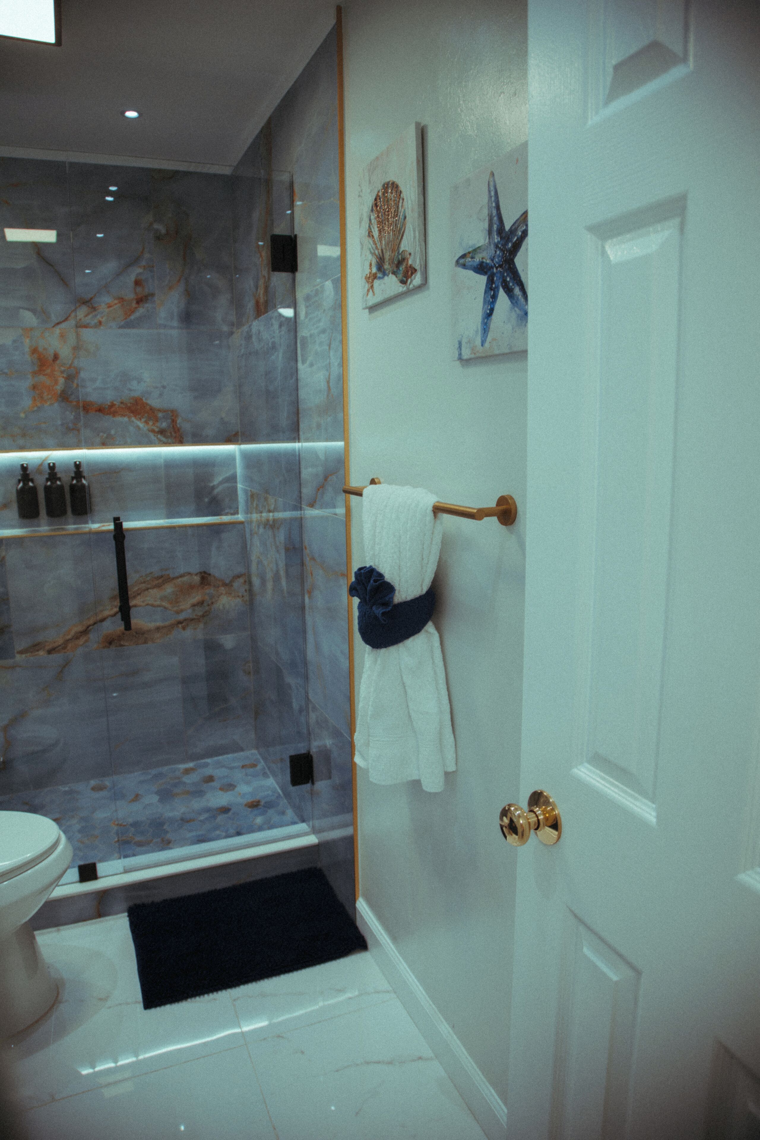 A bathroom with a glass-enclosed shower, a white toilet, and a towel rack with a blue towel.
