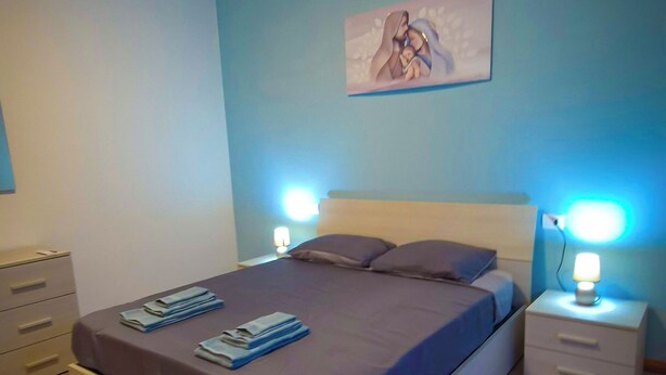 A bedroom with a bed, two bedside tables, a nightstand, a wall-mounted artwork, and a wooden floor.