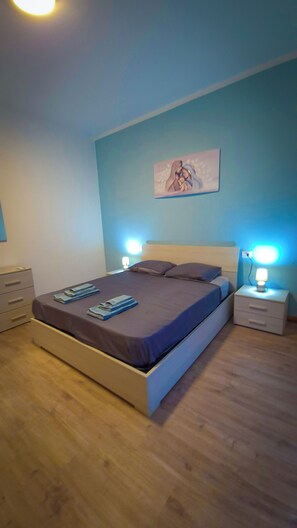 Une chambre à coucher comprenant un lit, deux tables de chevet, une commode, une œuvre d’art accrochée au mur et un plancher en bois.