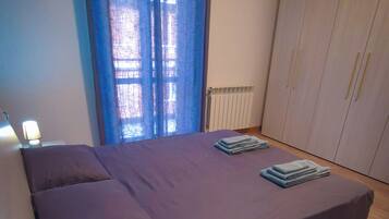 Ein Schlafzimmer mit einem Bett, einem Nachttisch mit Lampe, einem Kleiderschrank und einem Fenster mit Vorhängen.