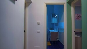 A narrow hallway with a wooden floor leading to a bathroom with a blue-tiled floor.