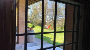 Blick durch ein fensterartiges Gitter auf ein Ziegelgebäude, eine Rasenfläche und einen Spielplatz mit bunten Geräten.