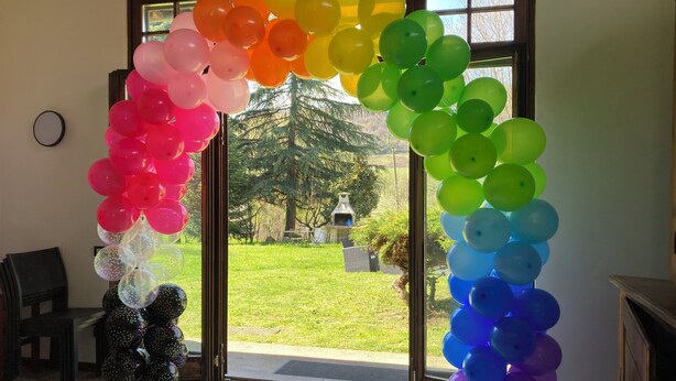 Ein Zimmer mit einer großen Glastür, die zu einem Garten führt, verziert mit einer bunten Girlande aus Ballons.
