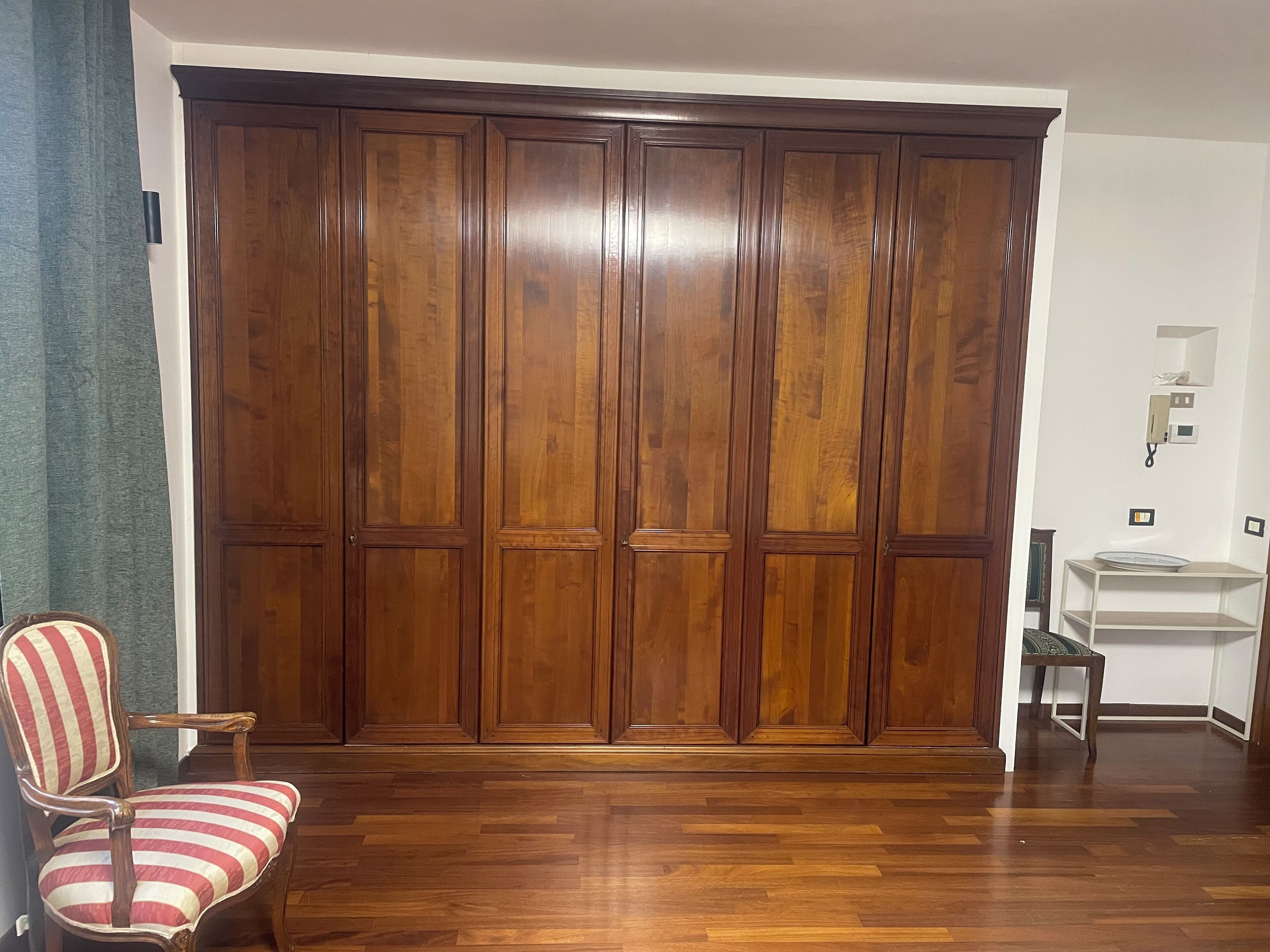 A room with a wooden wardrobe, a striped chair, and a small table.