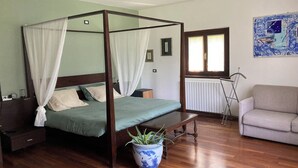Ein Bett mit Baldachin, ein Blumentopf, eine Holzbank, eine Heizung und ein Sofa in einem Zimmer mit Holzböden und einem Fenster.