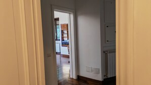 A hallway with a wooden floor leading to a room with a bed and a window.