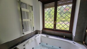 A bathroom with a bathtub, a window with a view of greenery, and a towel rack.