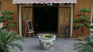 A traditional building entrance with a wooden facade, a large decorative ceramic pot with a lotus flower, and potted plants. - Ningbo Ivory Guest Youth Hostel (Ningbo)