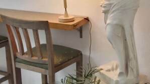 A wooden chair with a cushion, a desk with a lamp, and a statue on a pedestal. - Ningbo Ivory Guest Youth Hostel (Ningbo)