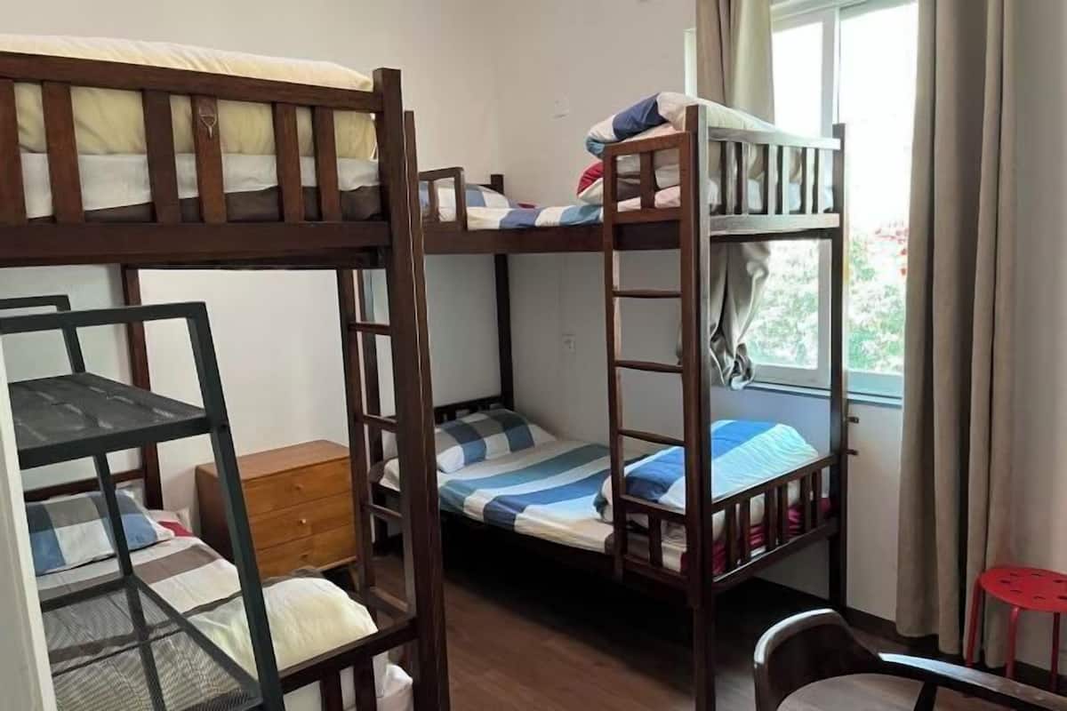 A room with three bunk beds, a wooden dresser, and a window with curtains.