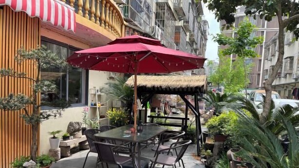 An outdoor seating area with a table and chairs, surrounded by potted plants and a red umbrella. - Ningbo Ivory Guest Youth Hostel (Ningbo)