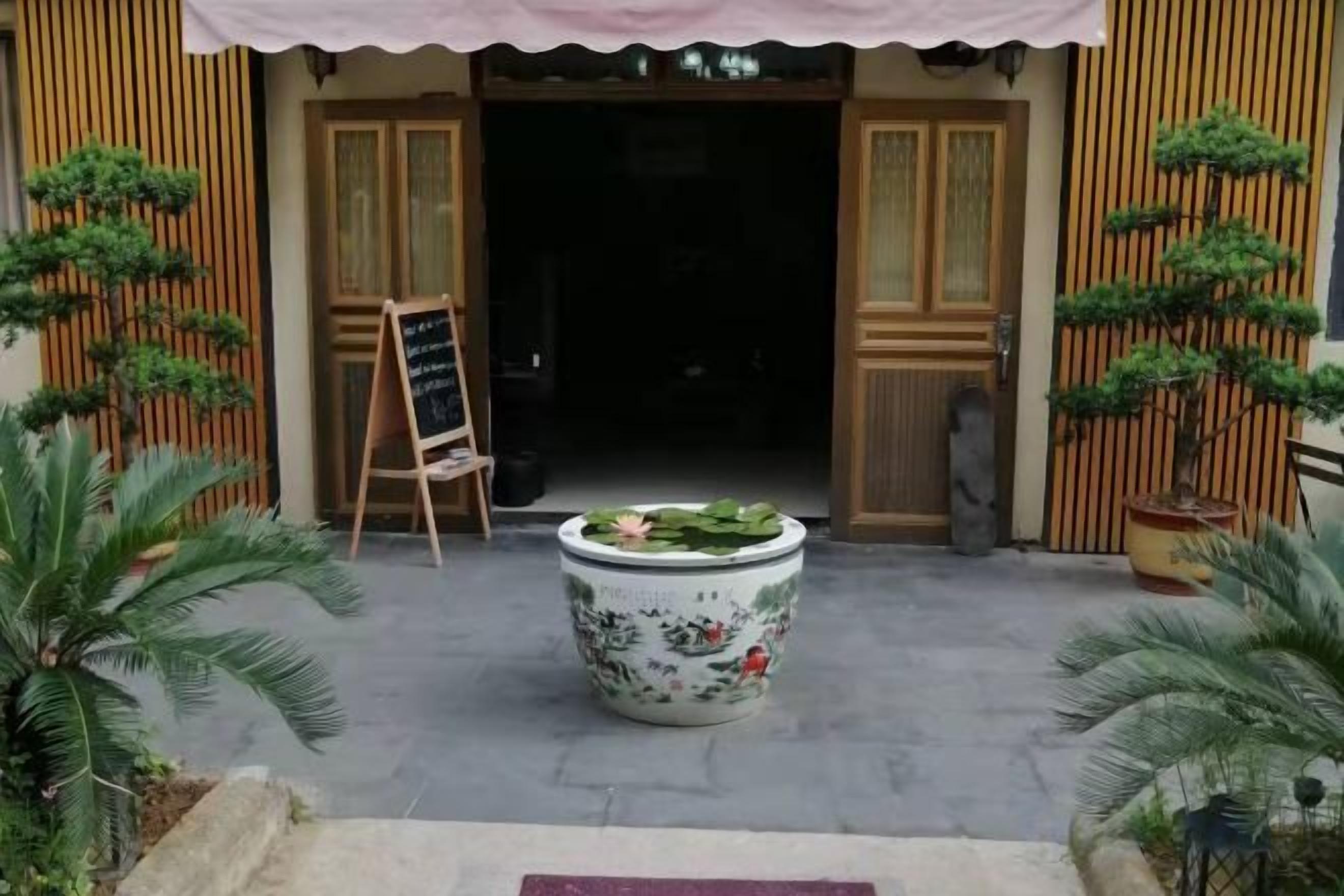 A traditional building entrance with a large potted plant, wooden doors, and a signboard.