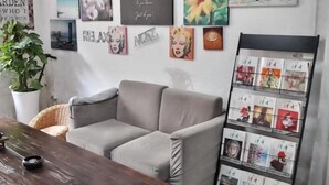A living room with a grey sofa, a coffee table, and a wall decorated with various framed pictures and a vertical photo album. - Ningbo Ivory Guest Youth Hostel (Ningbo)