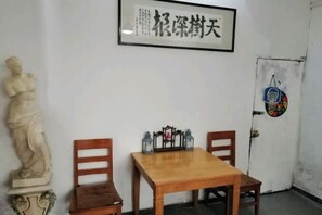 A room with a wooden table and chairs, a statue, and a framed artwork on the wall. - Ningbo Ivory Guest Youth Hostel (Ningbo)