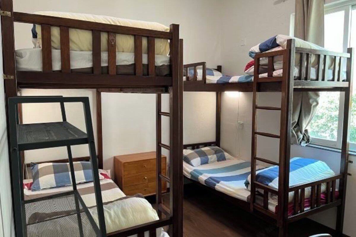 A bunk bed room with a wooden dresser and a window with curtains.