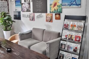A room with a grey sofa, a wooden table, a potted plant, and a wall with various framed pictures and a bulletin board. - Ningbo Ivory Guest Youth Hostel (Ningbo)