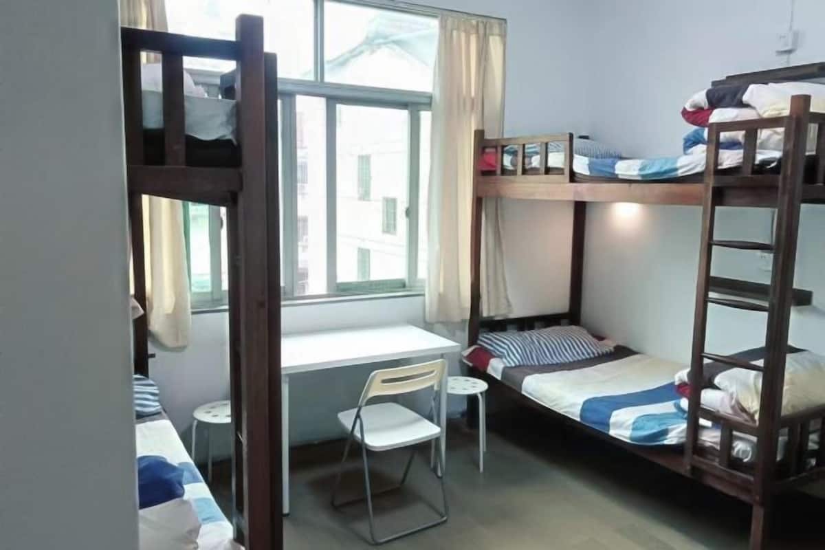 A dormitory room with bunk beds, a desk, a chair, and a window.