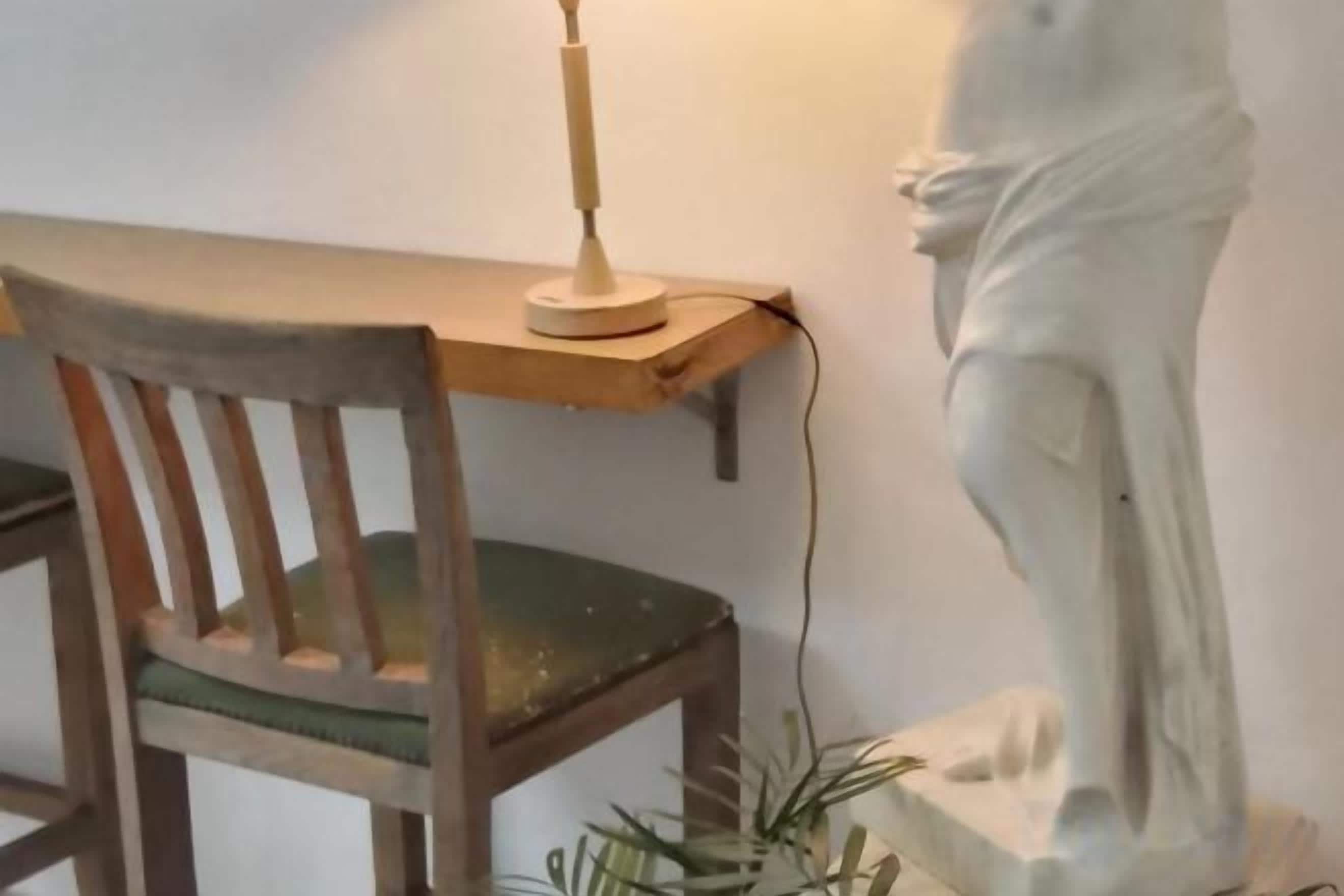 Una silla de madera con cojín, un escritorio con lámpara y una estatua.