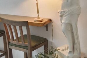 Une chaise en bois avec un coussin, un bureau avec une lampe et une statue.