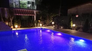A swimming pool with steps leading into it, surrounded by potted plants and a building with a balcony.