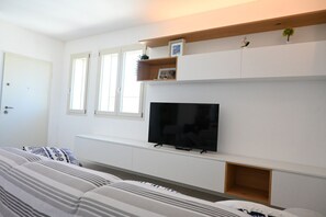 Ein Wohnzimmer mit einer Couch, einem flachbildfernseher an der Wand und einem Fenster mit Jalousien.