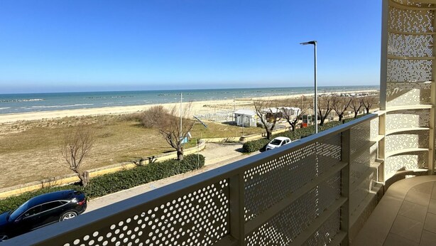 Un balcón con vista a la playa, una farola y coches aparcados.