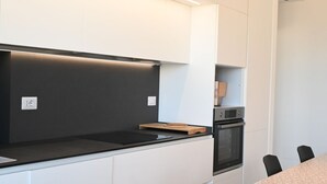 Una cocina moderna con armarios blancos, encimera negra y horno empotrado.