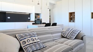 Una sala de estar moderna con un sofá, almohadas y una cocina al fondo.