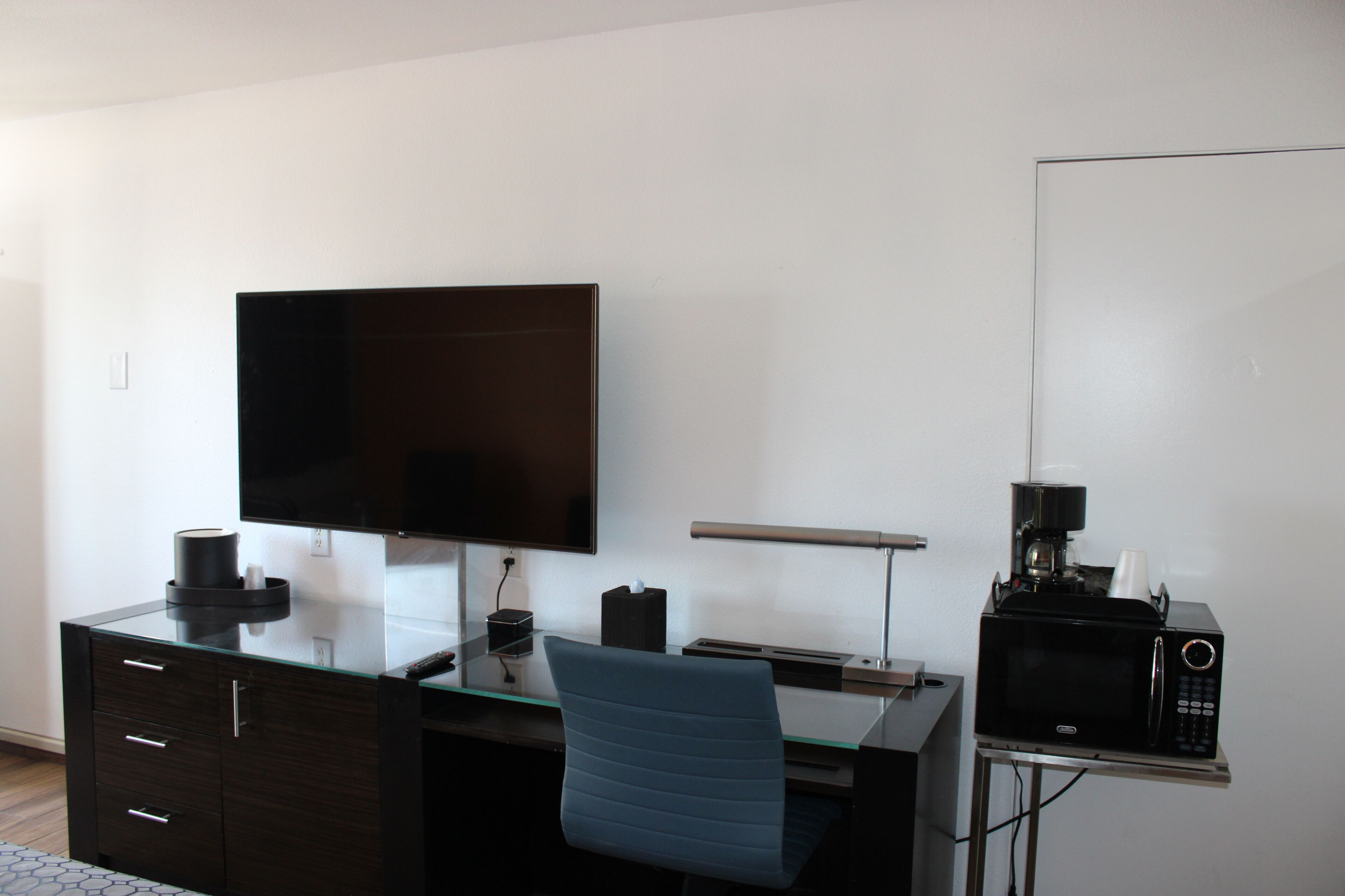 Een moderne kantoorruimte met een bureau, stoel, flatscreen televisie, koffiezetapparaat en magnetron.