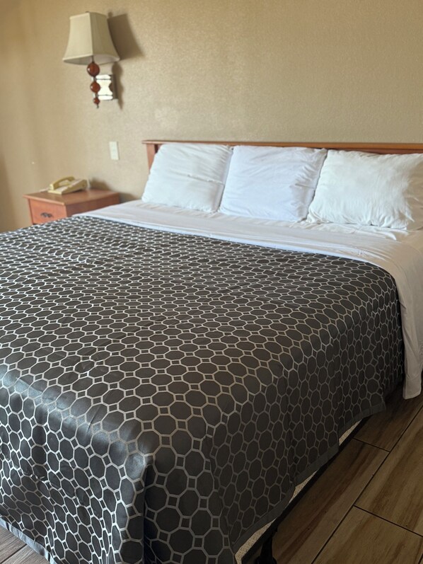 A neatly made bed with a patterned bedspread, a wooden headboard, a bedside table with a lamp, and a telephone on the nightstand.