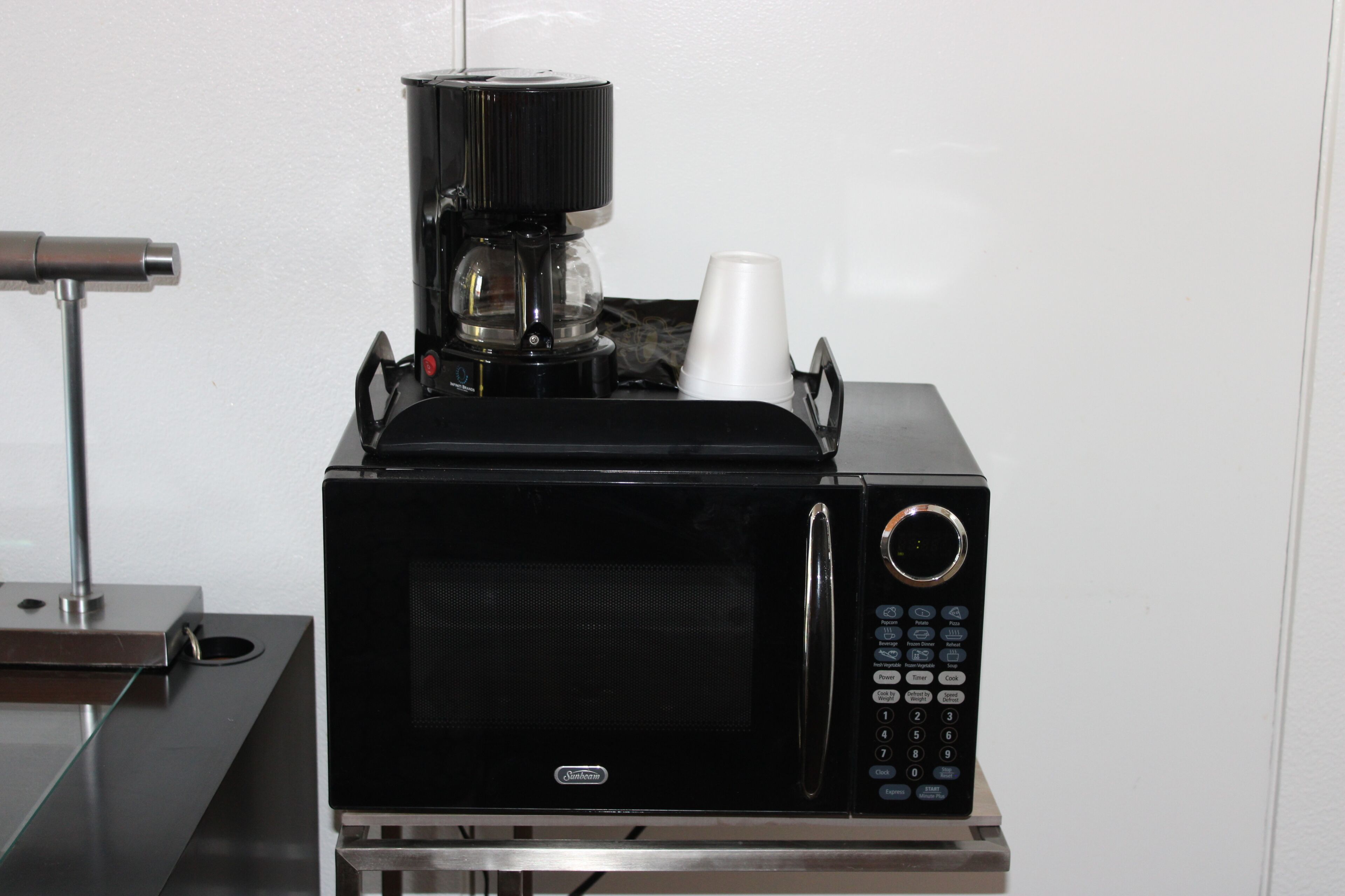 A black microwave with a coffee maker on top, a cup holder, and a control panel with buttons.