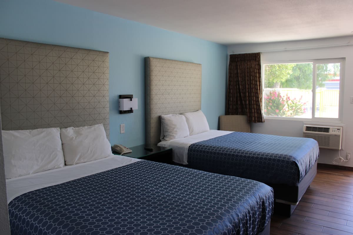 Une chambre d’hôtel avec deux lits, une fenêtre avec des rideaux, un appareil de climatisation et un téléphone fixé au mur.