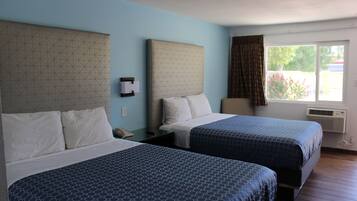 A hotel room with two beds, a window with curtains, an air conditioning unit, and a wall-mounted telephone.