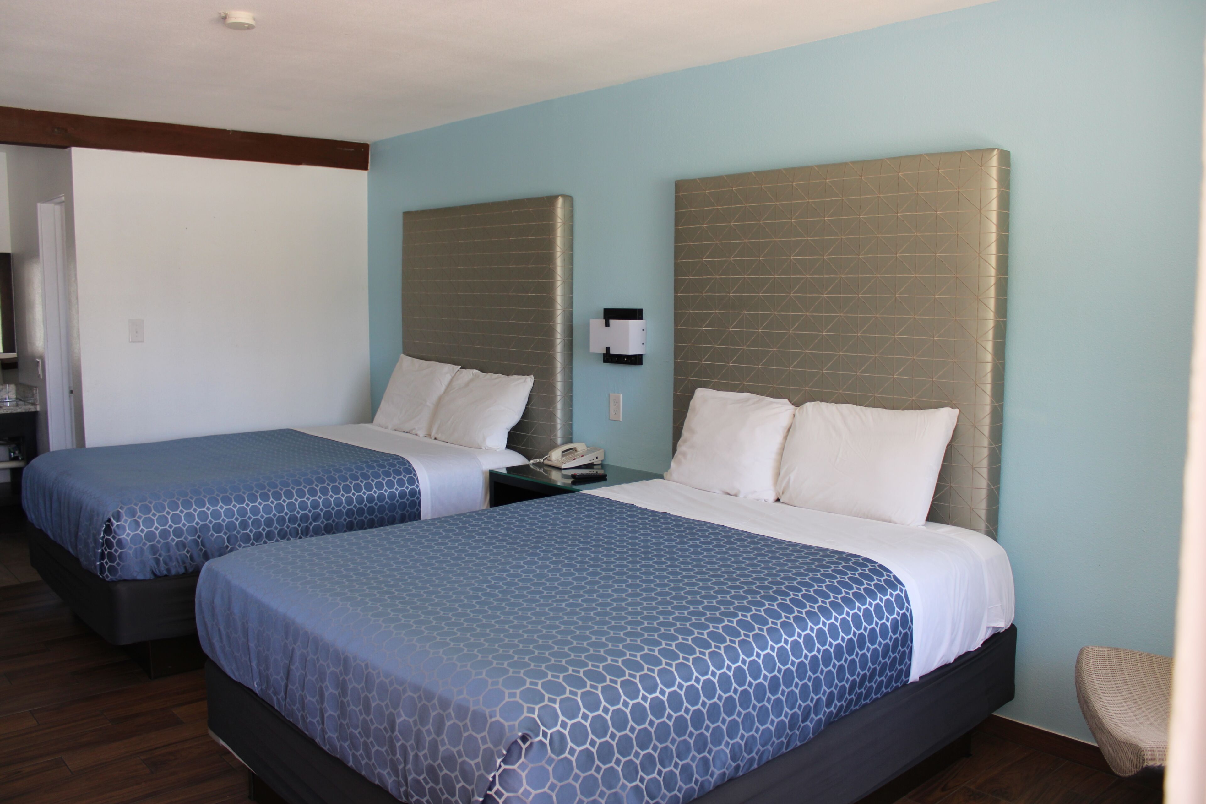 Two twin beds with headboards, a bedside table with a phone, and a chair in a room with light blue walls and wooden flooring.