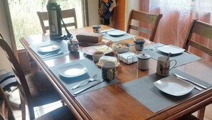 A dining table set with plates, bowls, cups, and cutlery, surrounded by chairs. - Hostal Nahuel Ray (Pucon)