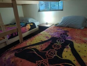 A bunk bed room with a colorful bedspread, a small bedside table, and a window above the bed. - Hostal Nahuel Ray (Pucon)