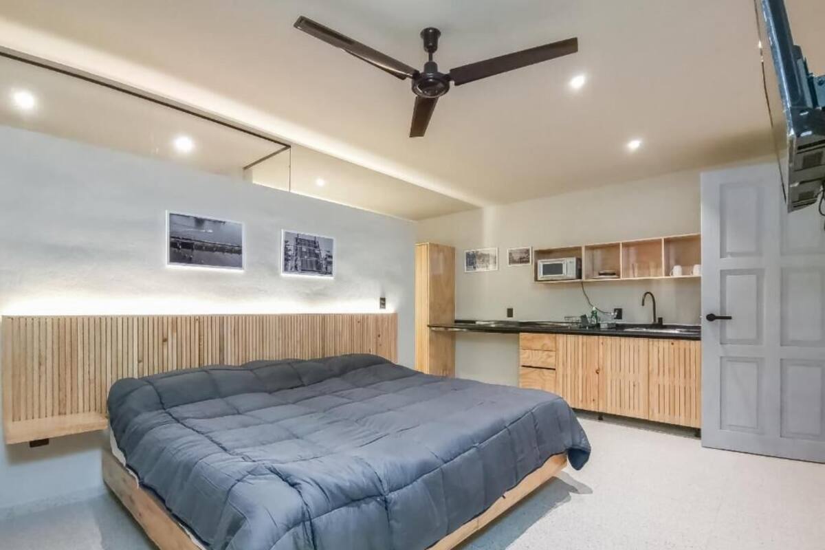 A bedroom with a bed, a ceiling fan, and a kitchenette with a microwave.