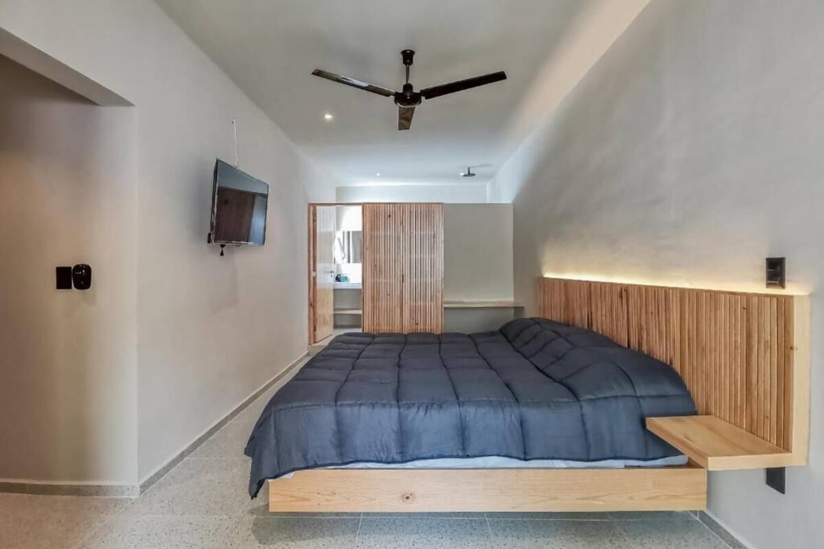 A modern bedroom with a bed, wooden headboard, ceiling fan, and a TV mounted on the wall.