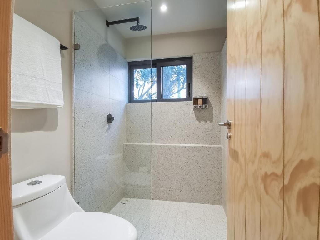 Une salle de bain moderne avec une douche à parois de verre, des toilettes et une petite fenêtre.