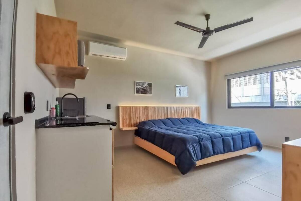 A bedroom with a bed, a desk, a ceiling fan, and a window.