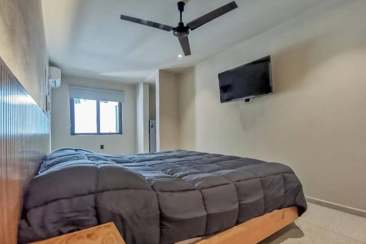 A bedroom with a bed, a ceiling fan, a TV, and a window.