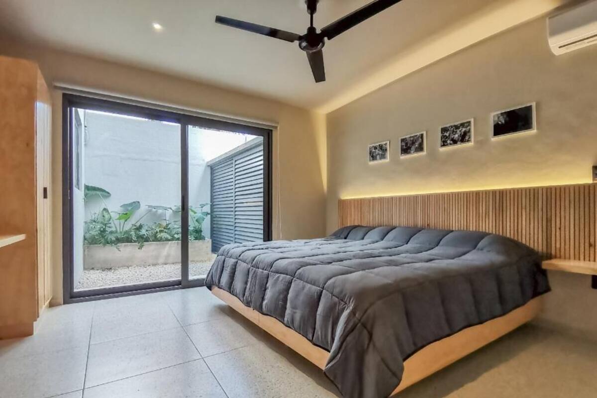 A modern bedroom with a large bed, sliding glass doors to a balcony, and a ceiling fan.