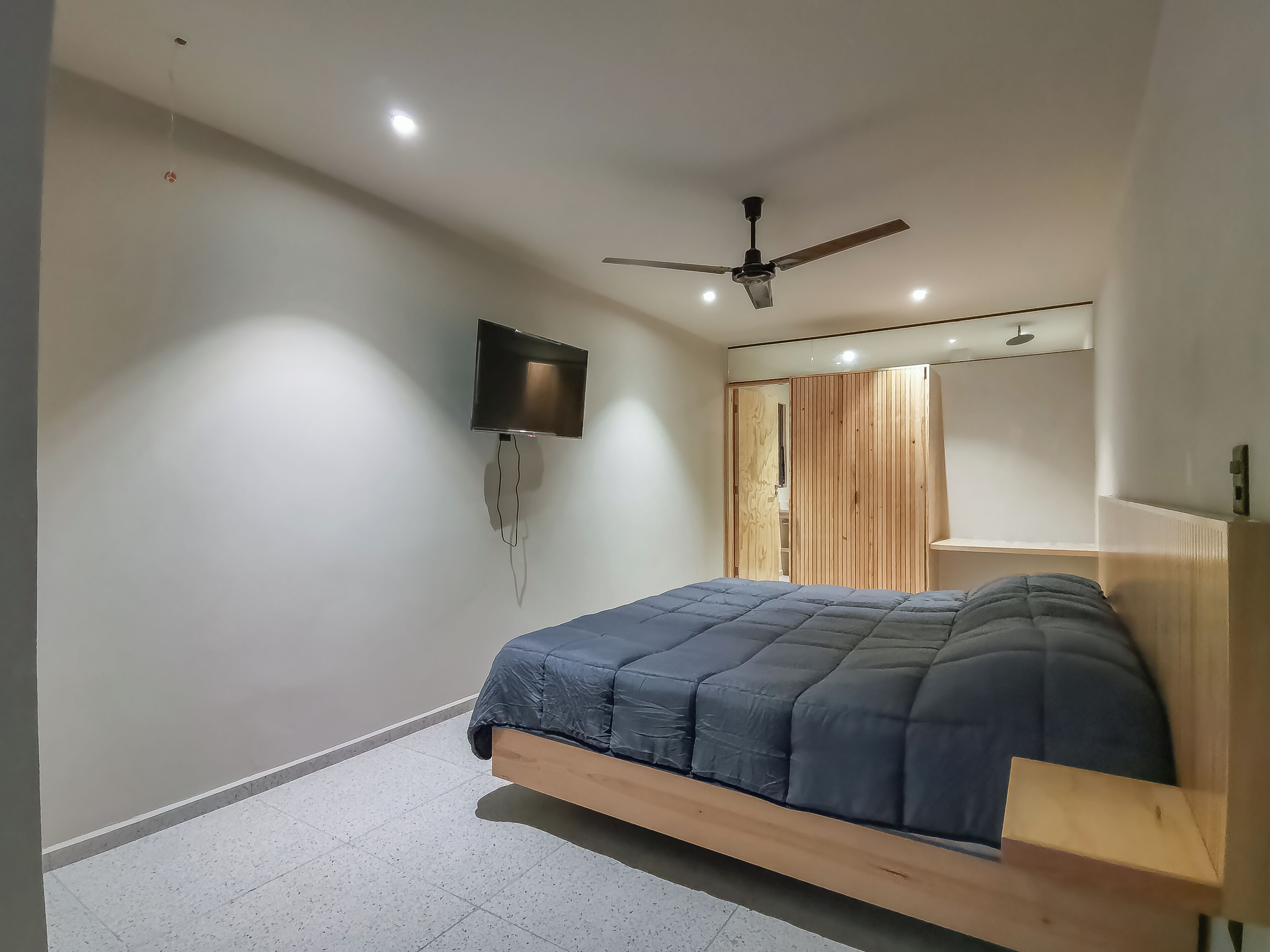 A modern bedroom with a bed, a ceiling fan, recessed lighting, a TV, and a wooden wardrobe.