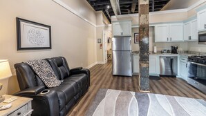 Um apartamento moderno com sala de estar, que inclui um sofá de couro, cozinha com eletrodomésticos de aço inoxidável e dutos de teto expostos.