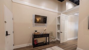 A hallway with a wooden floor, a console table with decorative items, a television mounted on the wall, and a chair. - Only Groundfloor access Downtown Laurel - G (Laurel)