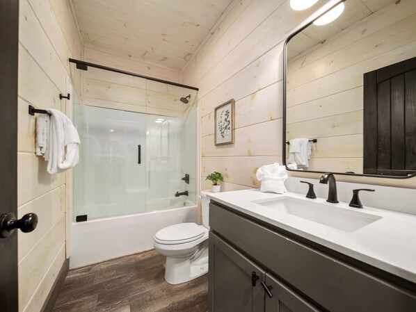 A modern bathroom with a glass-enclosed shower, a white toilet, a sink with three faucets, and a large mirror. - Million $ View|Pool Table|Indr Pool|Games (Sevierville)
