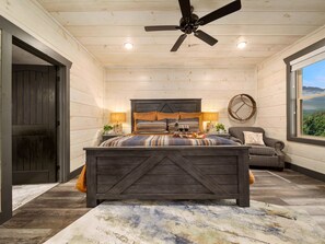 A bedroom with a wooden bed, a ceiling fan, a view of the outdoors through a window, and a rustic decor style. - Million $ View|Pool Table|Indr Pool|Games (Sevierville)