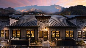 A modern two-story building with stone and metal roofing, large windows, and a view of mountains in the background. - 5min walk to Gatlinburg|Mtn View|Sauna|Indr Pool|Game| (Gatlinburg)